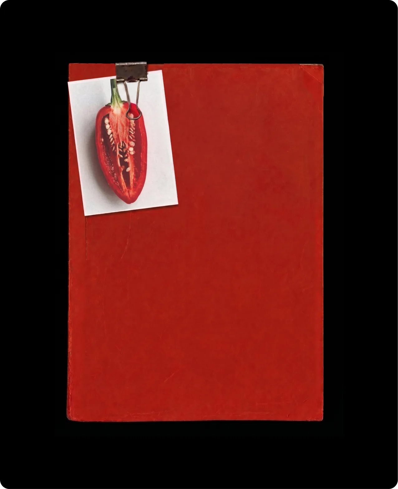 Heatwork: a red folder on black with a black bulldog clip holding a small card that shows a chilli halved lengthways