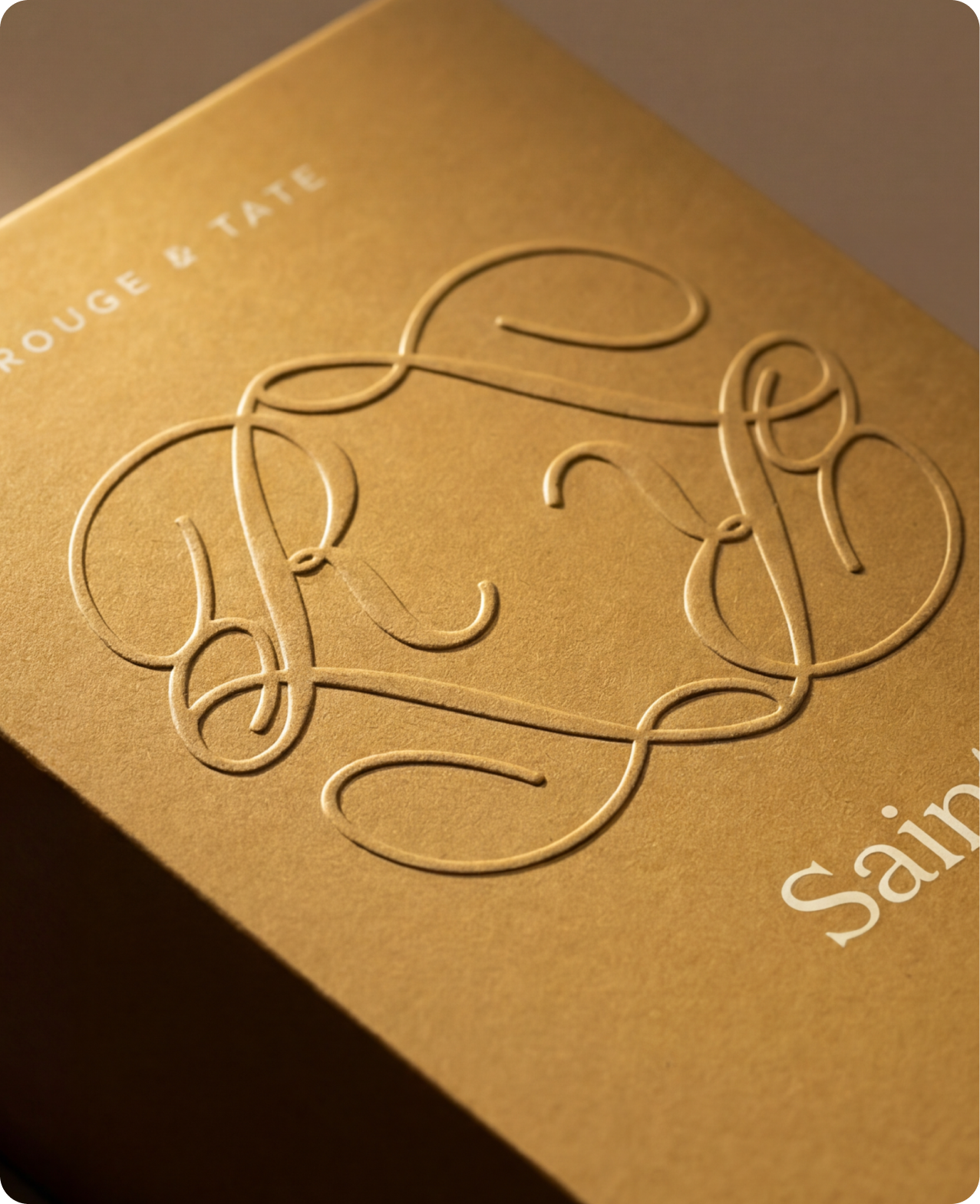 Rouge & Tate — macro on the Saint box, the R&T monogram embossed into gold cardstock