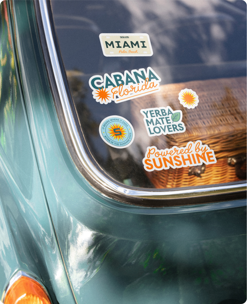 Sollos — the rear window of a vintage teal car covered in Sollos and beach-themed stickers, including Miami, Cabana, and Yerba Mate Lovers