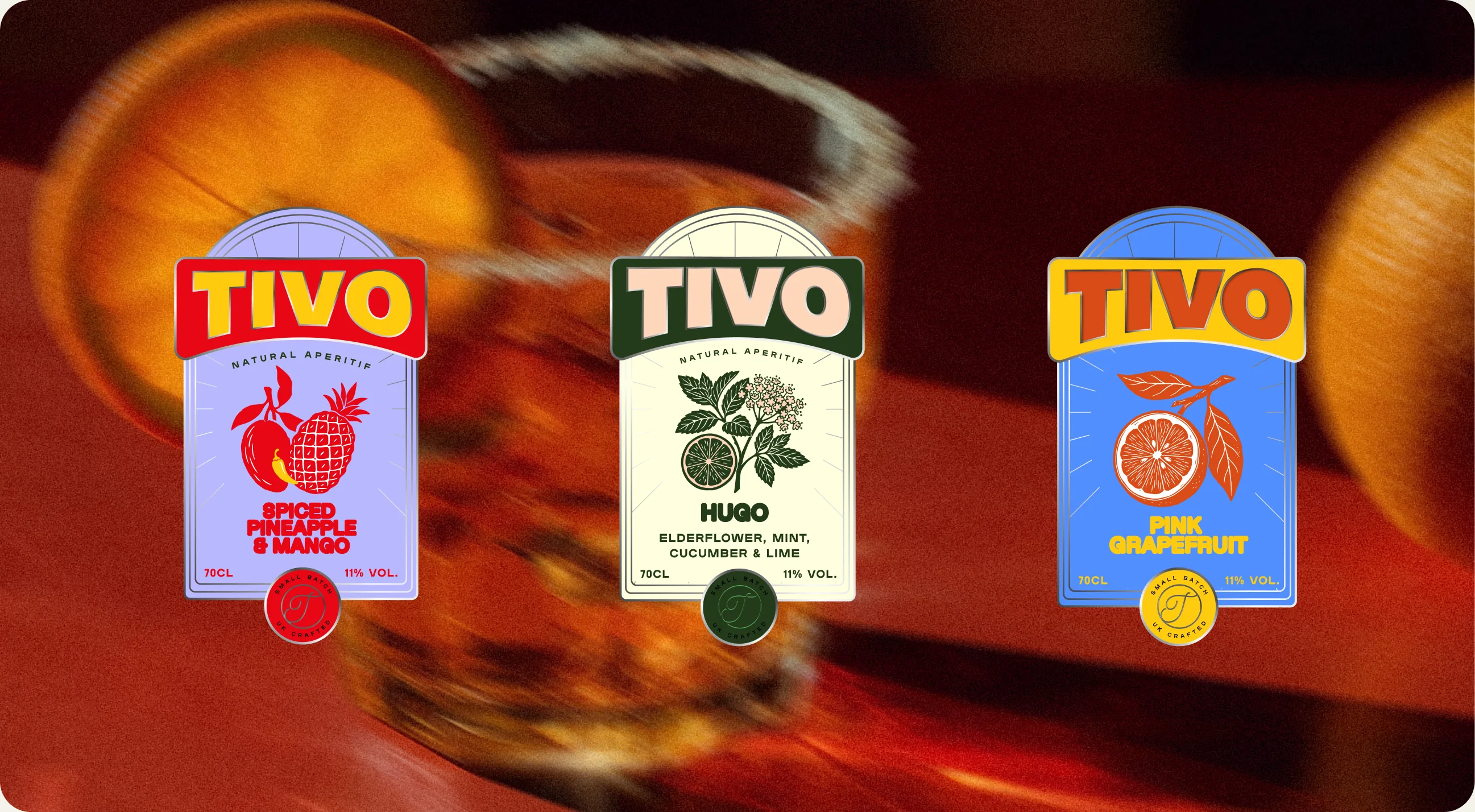 Tivo: the three bottle labels stood upright against a blurred amber drink, lilac Spiced Pineapple and Mango, cream Hugo, and blue Pink Grapefruit, each closed with its own coloured seal
