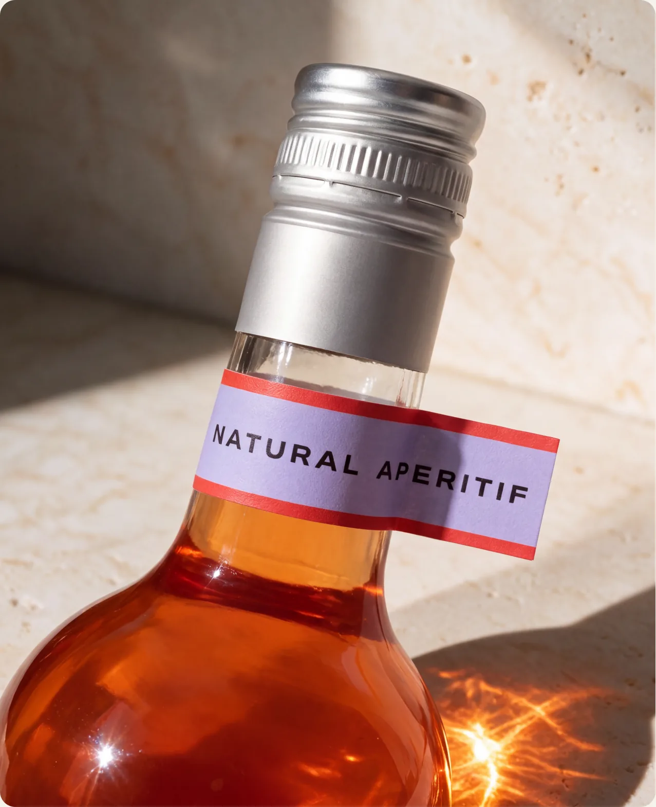 Tivo: a close-up of a bottle neck and brushed silver cap with a small natural aperitif label, lit from behind so the liquid glows