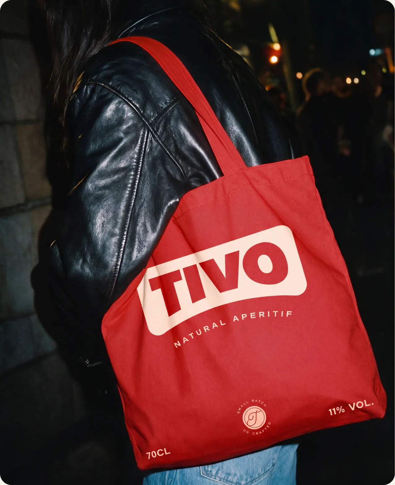 Tivo: a person in a black leather jacket carrying a red Tivo tote bag printed with the wordmark and the words natural aperitif