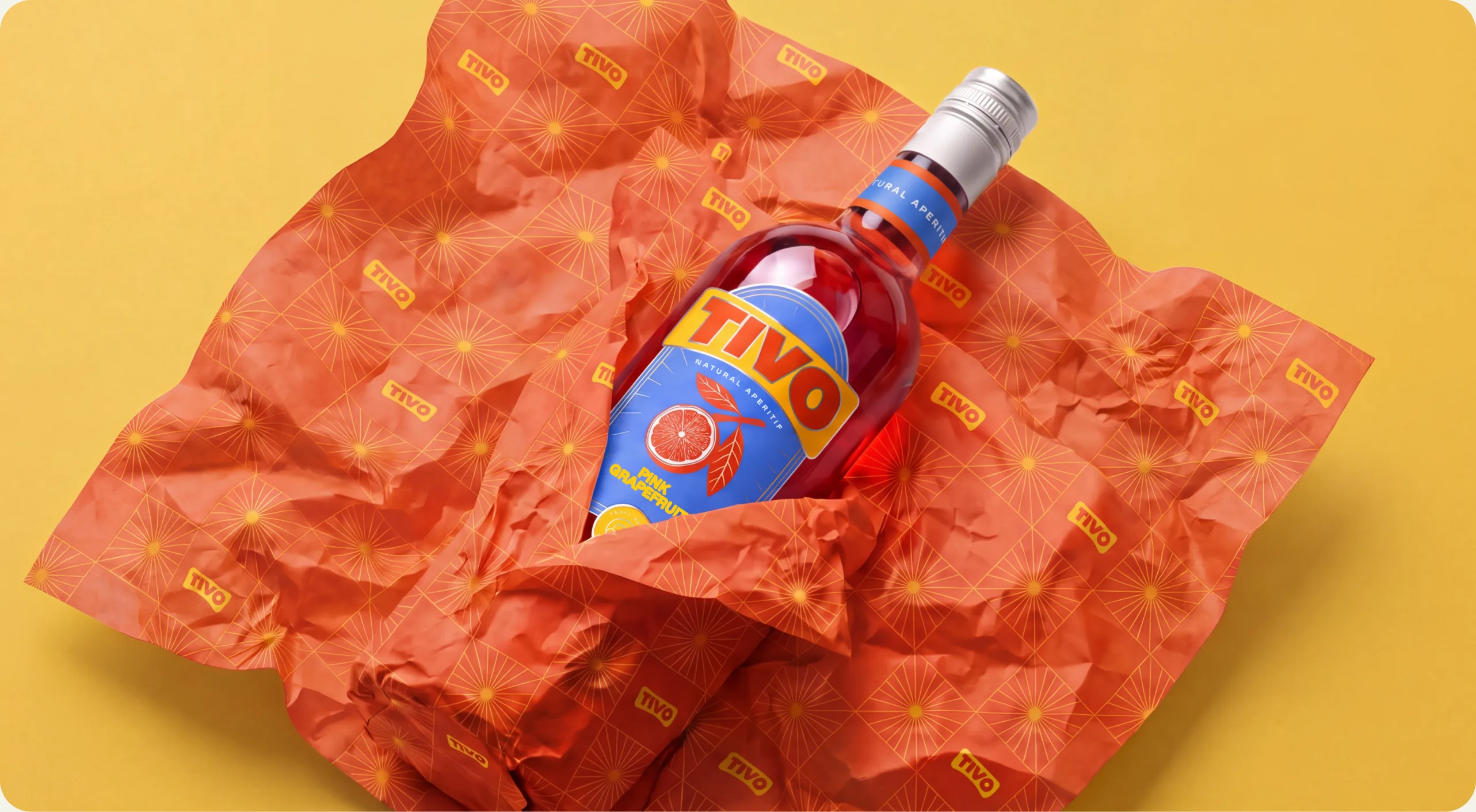 Tivo: a Pink Grapefruit bottle lying in crumpled orange tissue paper printed with the Tivo wordmark, on a yellow background