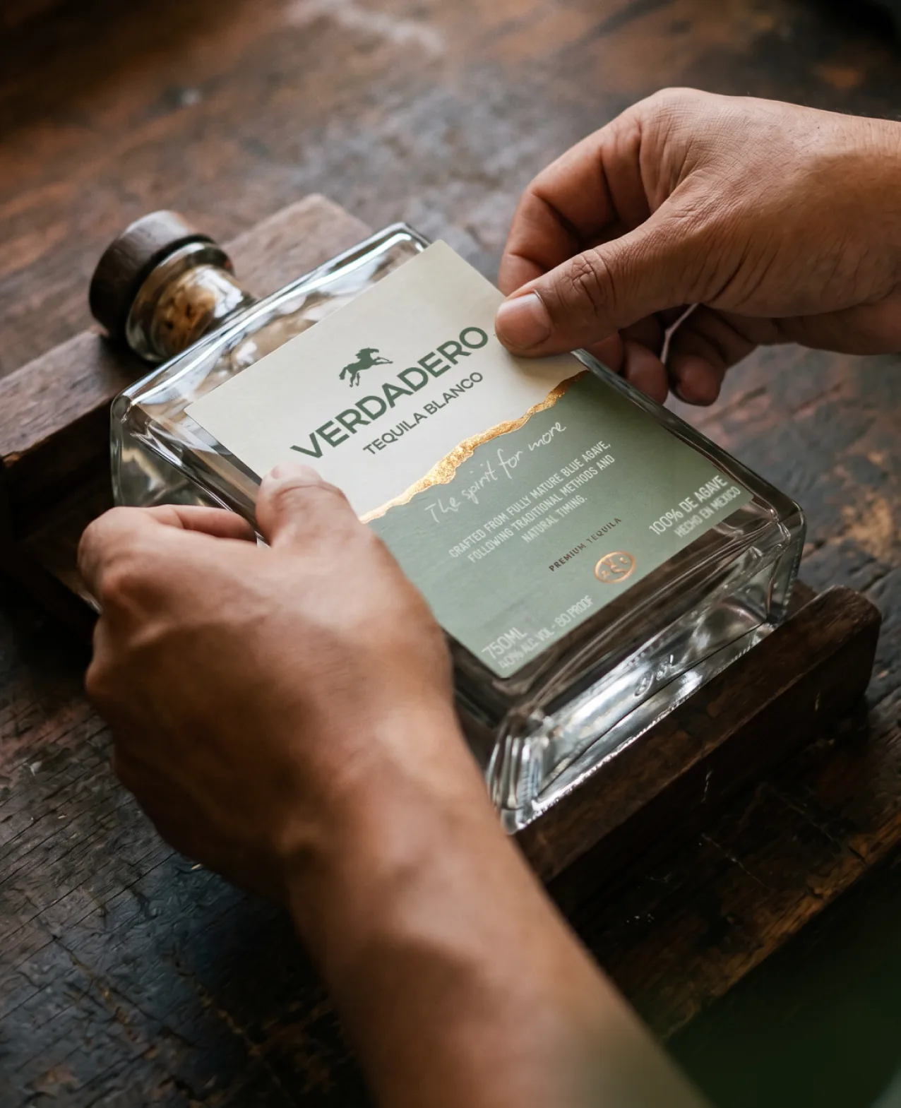 Verdadero — a hand holding the Blanco bottle over a wood table