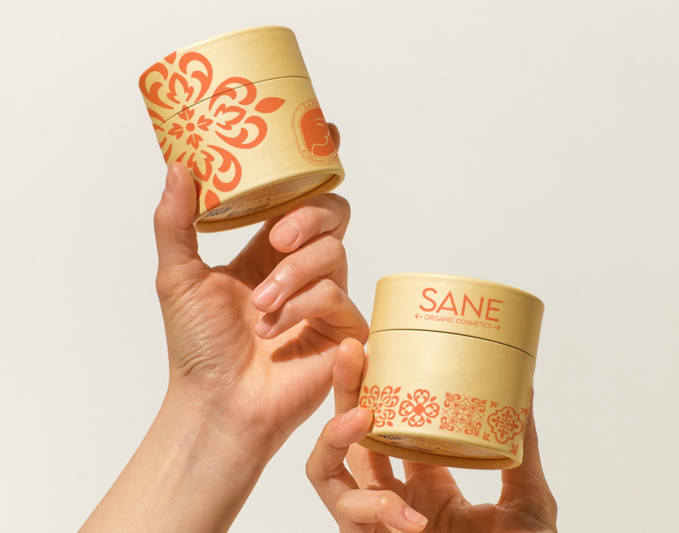 hands holding two organic cosmetic pots of cream. Made of cardboard in pastel colors, orange and yellow.