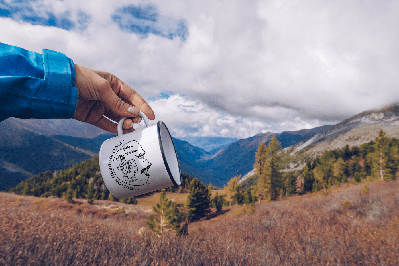 hand holding white metal mug with brand logo andname printed. Landscape background