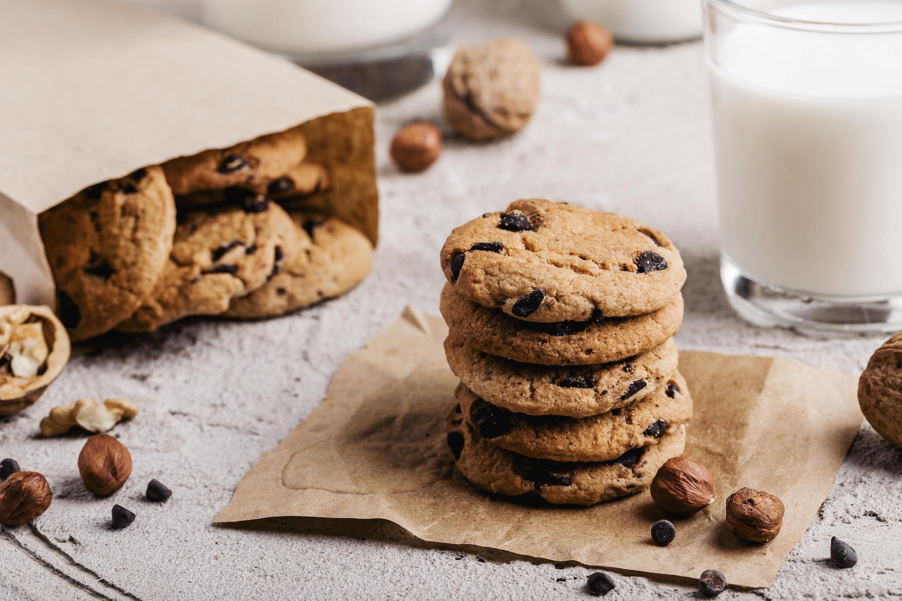 Delicious chocolate chip cookies. With a background in which you can see more cookies in a paper bag and a glass of milk