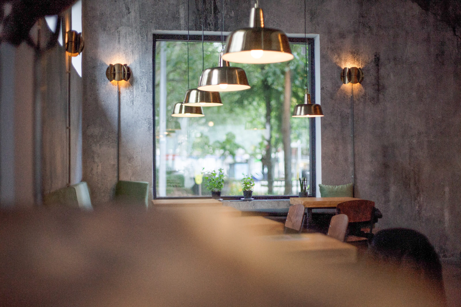 Cozy coffee shop with inviting wooden tables and comfortable chairs. Warm ambient lighting fills the space and a window that lets in natural light.